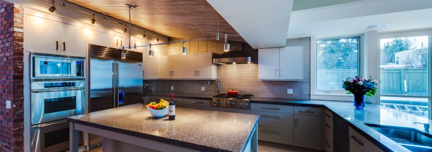 Midcentury modern kitchen with panelled ceiling, dark countertops, grey cabinetry and stainless steel appliances.