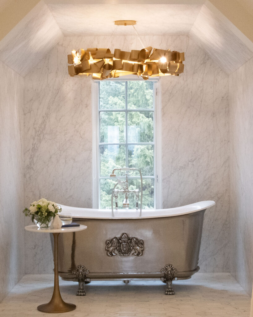 This luxurious ensuite has a stunning ribbon light fixture over an ornate claw foot tub in a modern castle in Springbank.