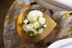 Fresh white flowers with green foliage on a gold teardrop shape table. Fresh flowers add a touch of hygge!