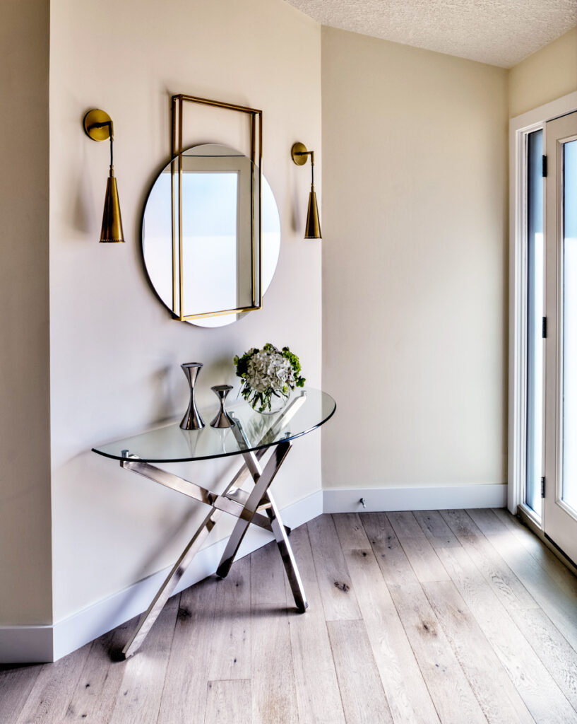 Mudroom blog - entryway with glass table and metallic base. Two brass sconces flank a unique mirror above the table.