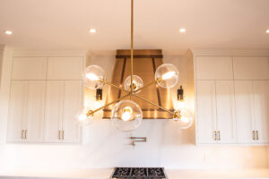 Villosa Ridge After - Planetary brass light fixture with globe lights in front of custom bronze hood fan with two tones of bronze.