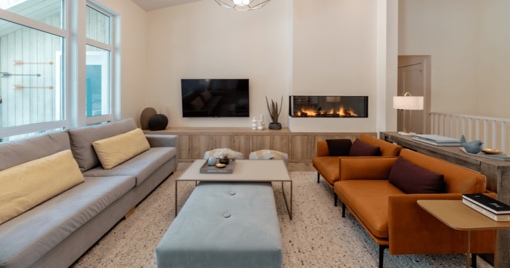 Scandinavian Design - Living room with orange accent chairs, light blue sofa and ottoman and clean lines dancing in the light of a soothing fireplace.