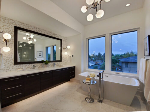 Ensuite bathroom with a standalone tub, floor-mounted faucet and a dark vanity flanked by globe lights.