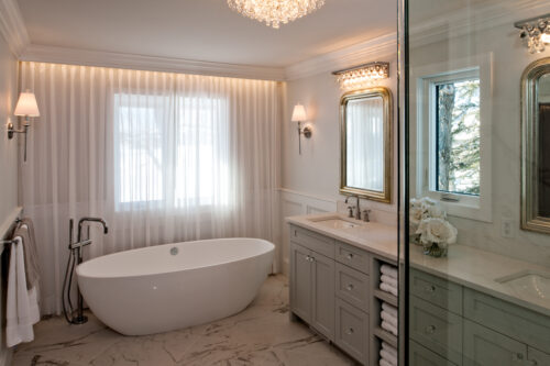 Glamorous luxury ensuite bathroom with sparkling chandeliers, an oval standalone tub and grey vanity.