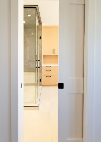 A pocket door allows entry to this ensuite bathroom complete with a steam shower, makeup vanity in a warm light wood, and standalone tub.