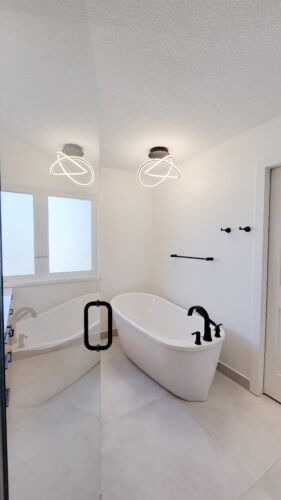 An artistic knot light shines above a standalone tub with striking black hardware in this ensuite bathroom.
