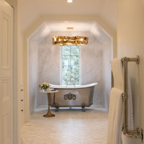 A bold copper ribbon light stands above a metal claw foot tub in a tile surrounded bathroom nook.