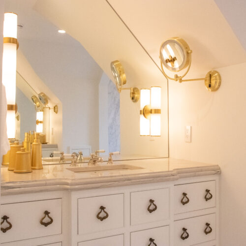 Warm gold vanity mirrors and lights illuminate a luxurious old-world white bathroom vanity.