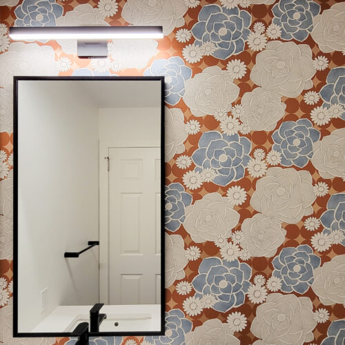 Powder room bathroom vanity mirror with fun orange, blue and brown floral wallpaper.