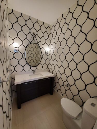 Powder room bathroom with black oval mirror, black vanity, and geometric wallpaper.