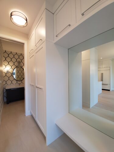 Mudroom white locker cabinets and sitting area leading to powder room bathroom with black vanity and oval mirror.