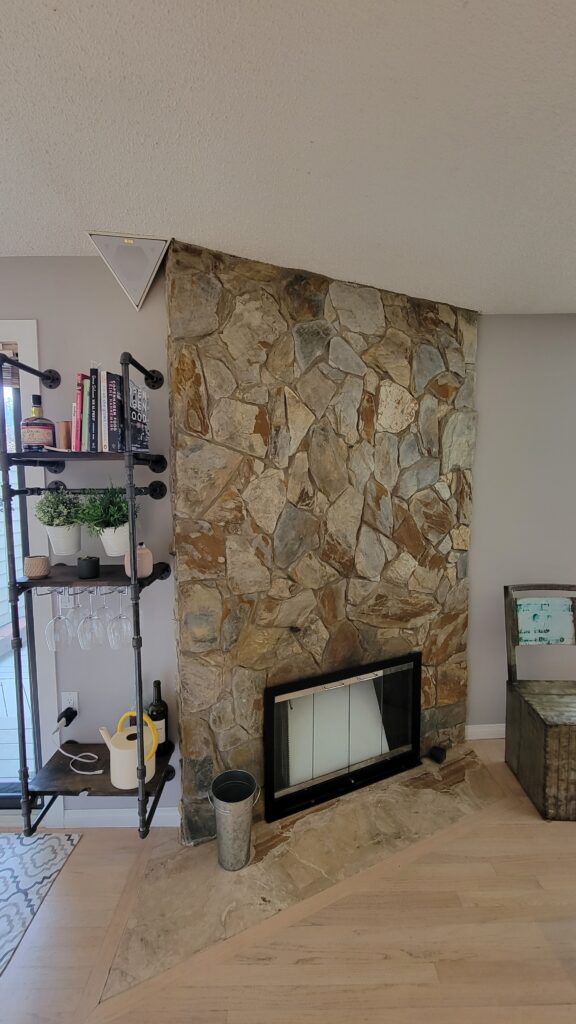 Before photo of fireplace that is faced with a mosaic of natural stone on a 45 degree angle. 
