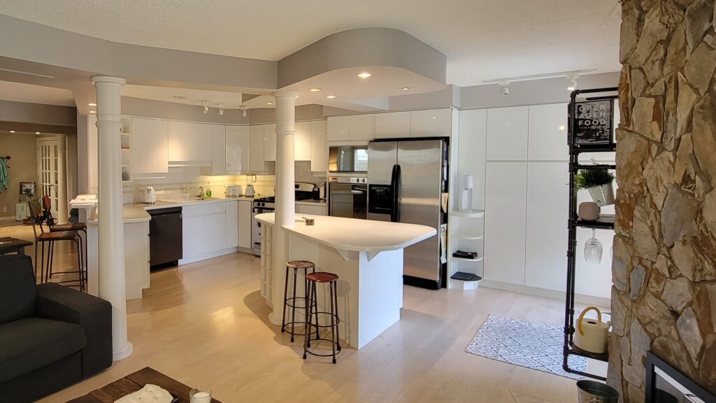 Kitchen construction before photo. The kitchen is white with an oddly shaped island and rounded bulkhead on the ceiling.