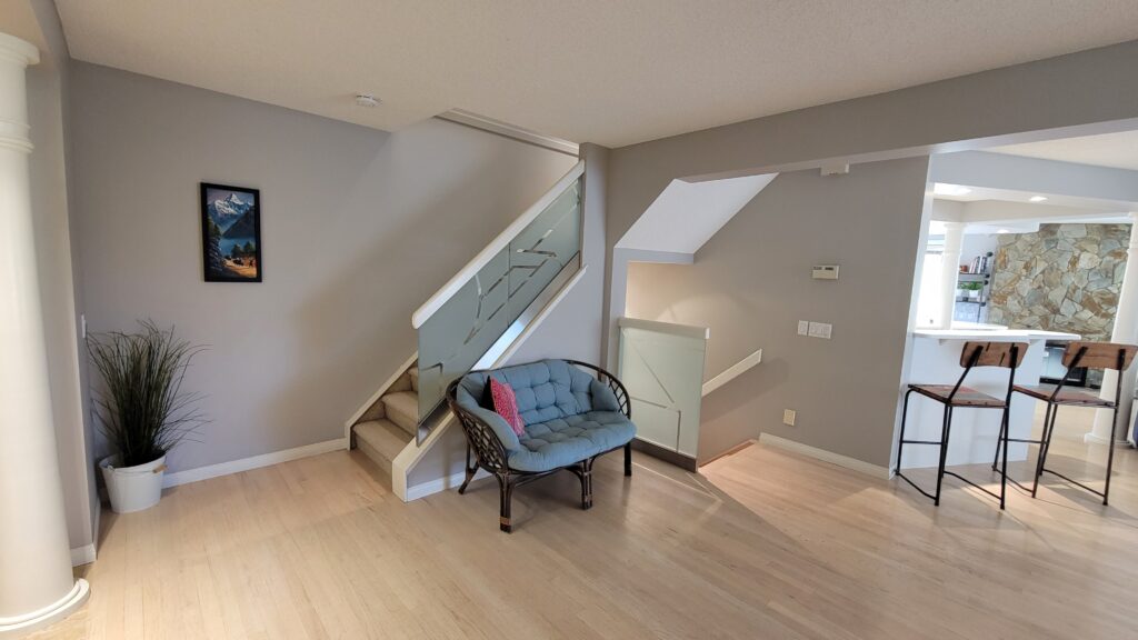 Before construction photo. The walls are grey and the glazing on the stairs is frosted with a design, the floor is a light maple colour, in the background you can see the white kitchen and the 1970s stone mosaic fireplace.