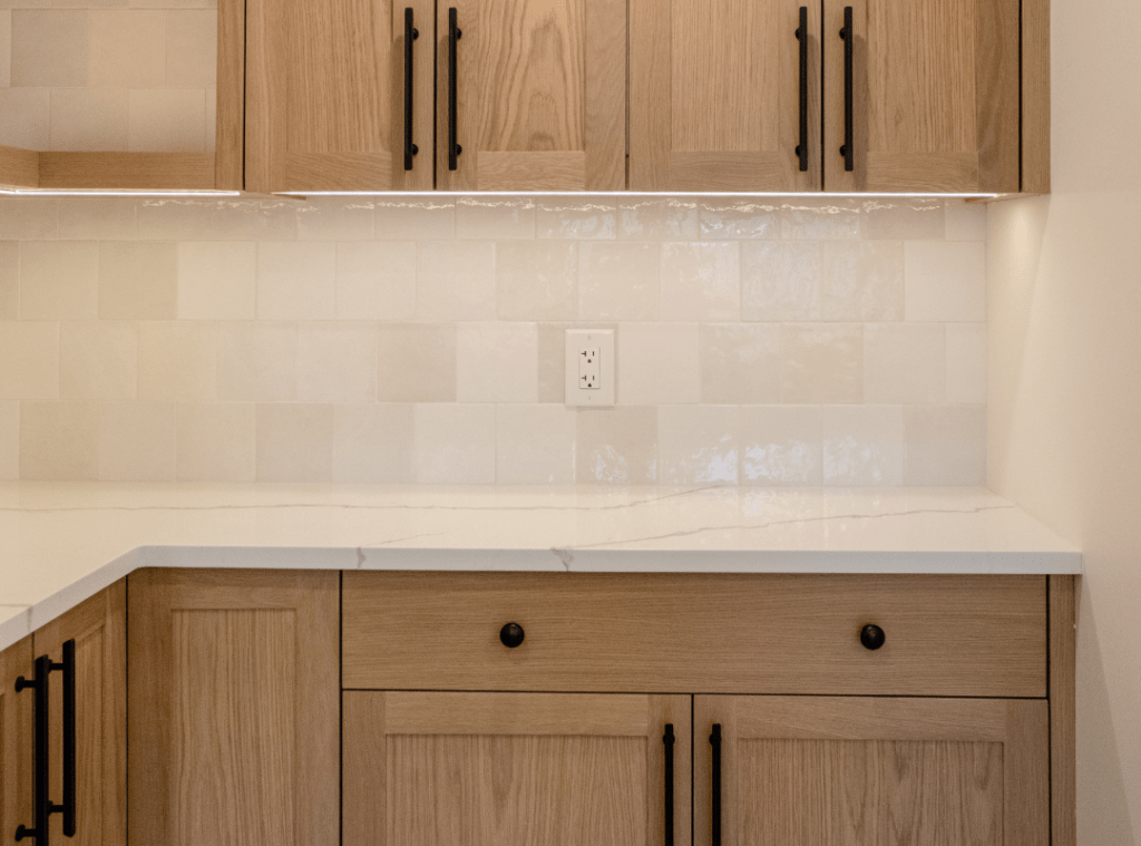 Light square textured tile with a shiny pearl finish backsplash, undermount lighting and light warm cabinets make this baker's nook a sneaky showstopper.