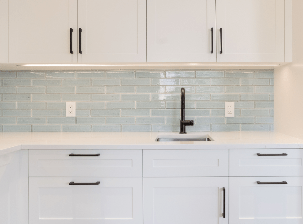 A matte black single handle faucet over a prep sink. Undermounted cabinet lights, veined countertops and blue artisan tile backsplash complete this look.