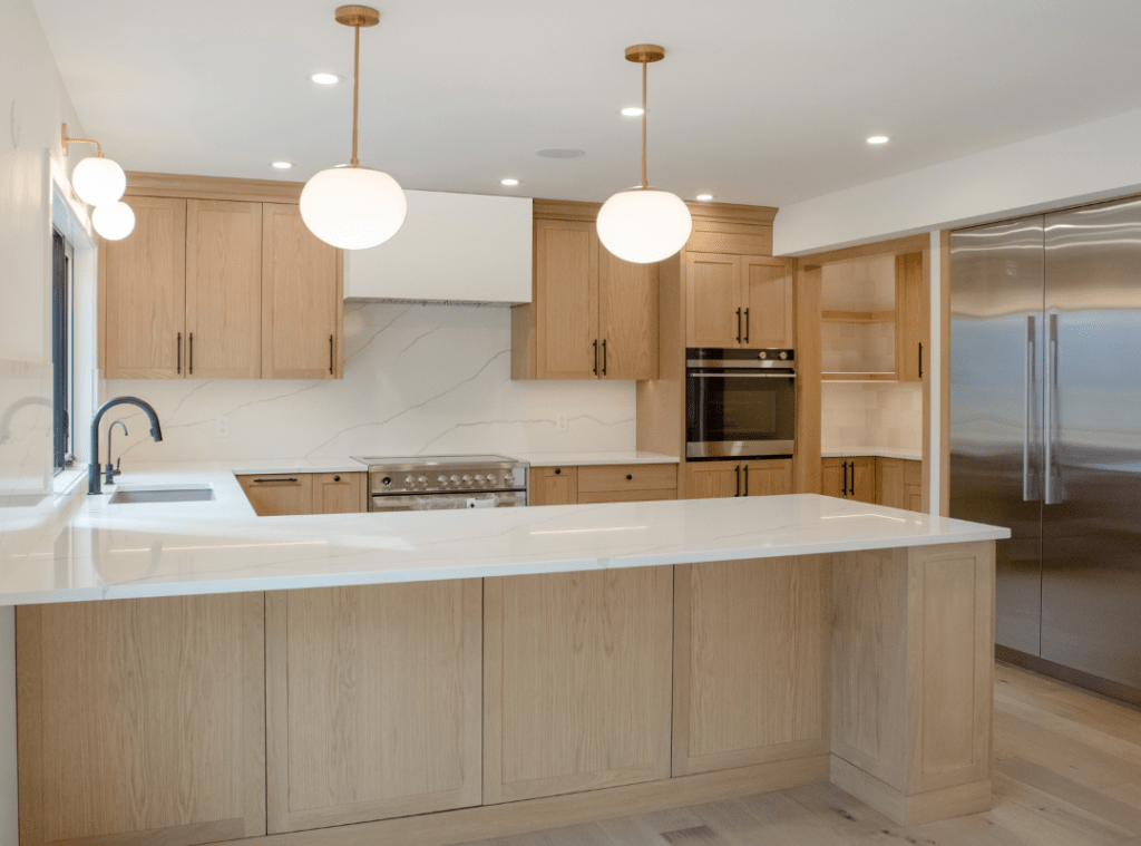 A bright spacious kitchen with light warm wood cabinets and light natural stone look countertops. Globe pendant lights, pot lights and a plastered hood fan finish off this look.