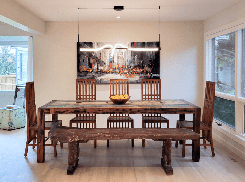 Rustic dining table with brightly coloured art behind. A linear rope light hangs above the dining table.